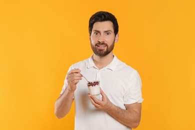 Photo of Handsome man with delicious yogurt and spoon on yellow background