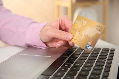 Photo of Online payment. Woman with credit card using laptop at table indoors, closeup
