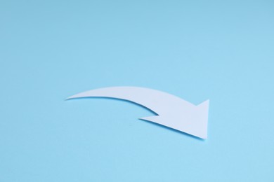 Photo of White curved paper arrow on light blue background