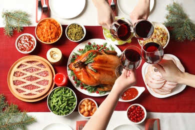 Women clinking glasses of wine over festive table with delicious roasted turkey, top view