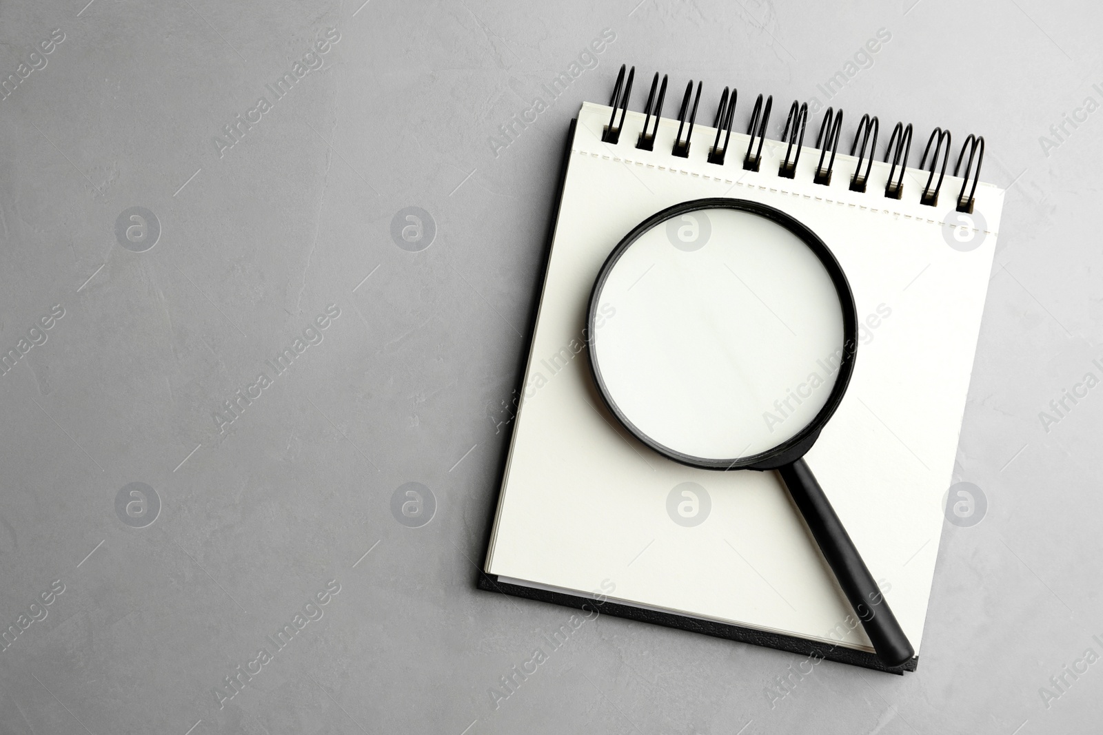 Photo of Top view of magnifier glass and empty notebook on light grey stone background, space for text. Find keywords concept