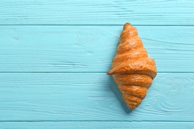 Photo of Tasty croissant and space for text on light blue wooden background, top view. French pastry