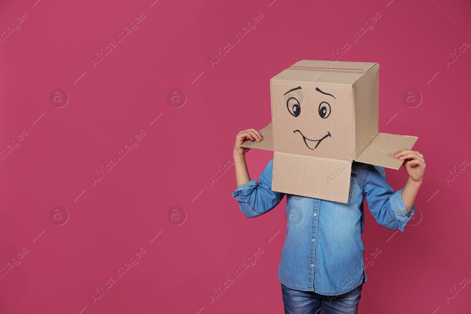 Photo of Cute little child wearing cardboard box with smiling face on color background. Space for text