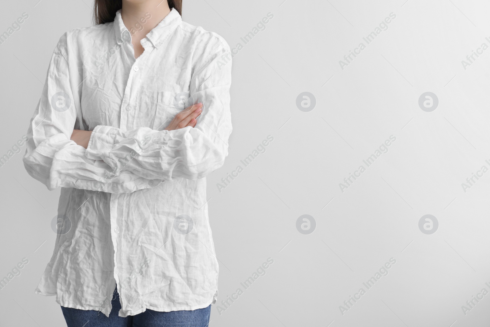 Photo of Woman wearing wrinkled white blouse on light grey background, closeup. Space for text