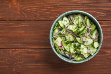 Photo of Delicious fresh cucumber onion salad in bowl on wooden table, top view. Space for text