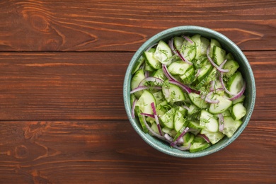 Delicious fresh cucumber onion salad in bowl on wooden table, top view. Space for text