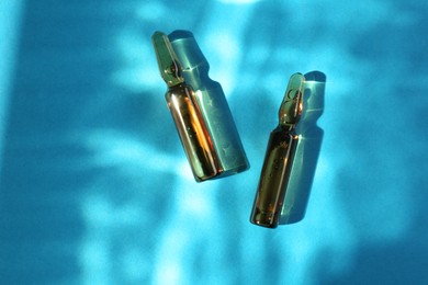 Photo of Skincare ampoules in sunlight on light blue background, top view