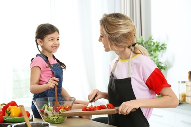 Young nanny with cute little girl cooking together in kitchen