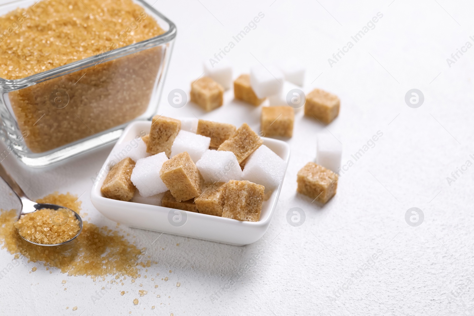 Photo of Bowls and spoon with different types of sugar on white table, closeup. Space for text