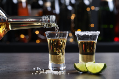 Photo of Pouring Mexican Tequila from bottle into shot glass on bar counter
