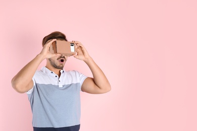 Photo of Young man using cardboard virtual reality headset on color background. Space for text