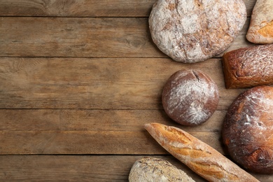 Different kinds of fresh bread on wooden table, flat lay. Space for text