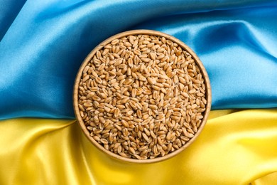 Bowl of wheat grains on Ukrainian flag, top view