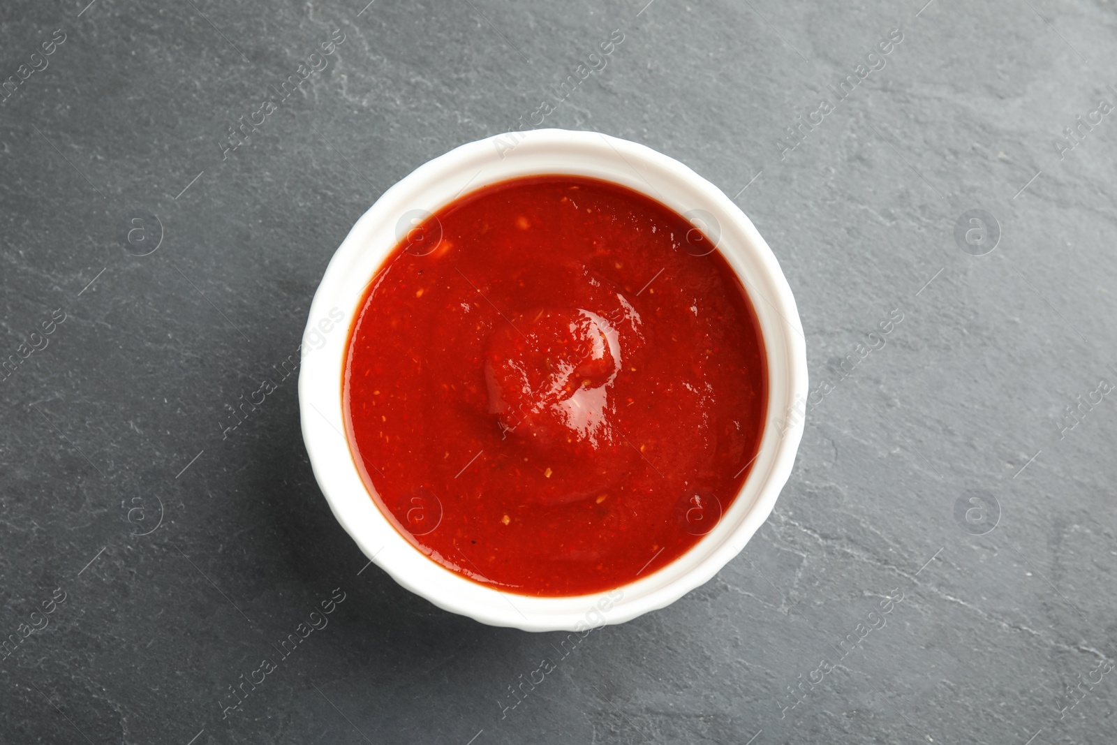 Photo of Bowl of tasty tomato sauce on grey table, top view