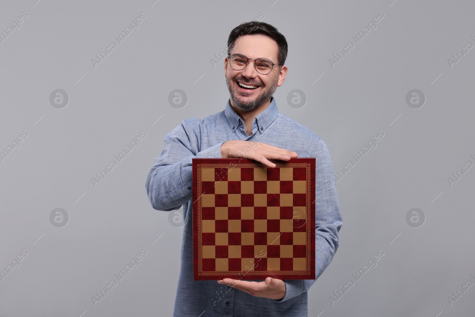 Photo of Smiling man holding chessboard on light grey background