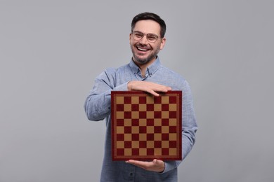 Smiling man holding chessboard on light grey background