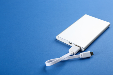 Photo of Modern portable charger with cable on blue background. Space for text