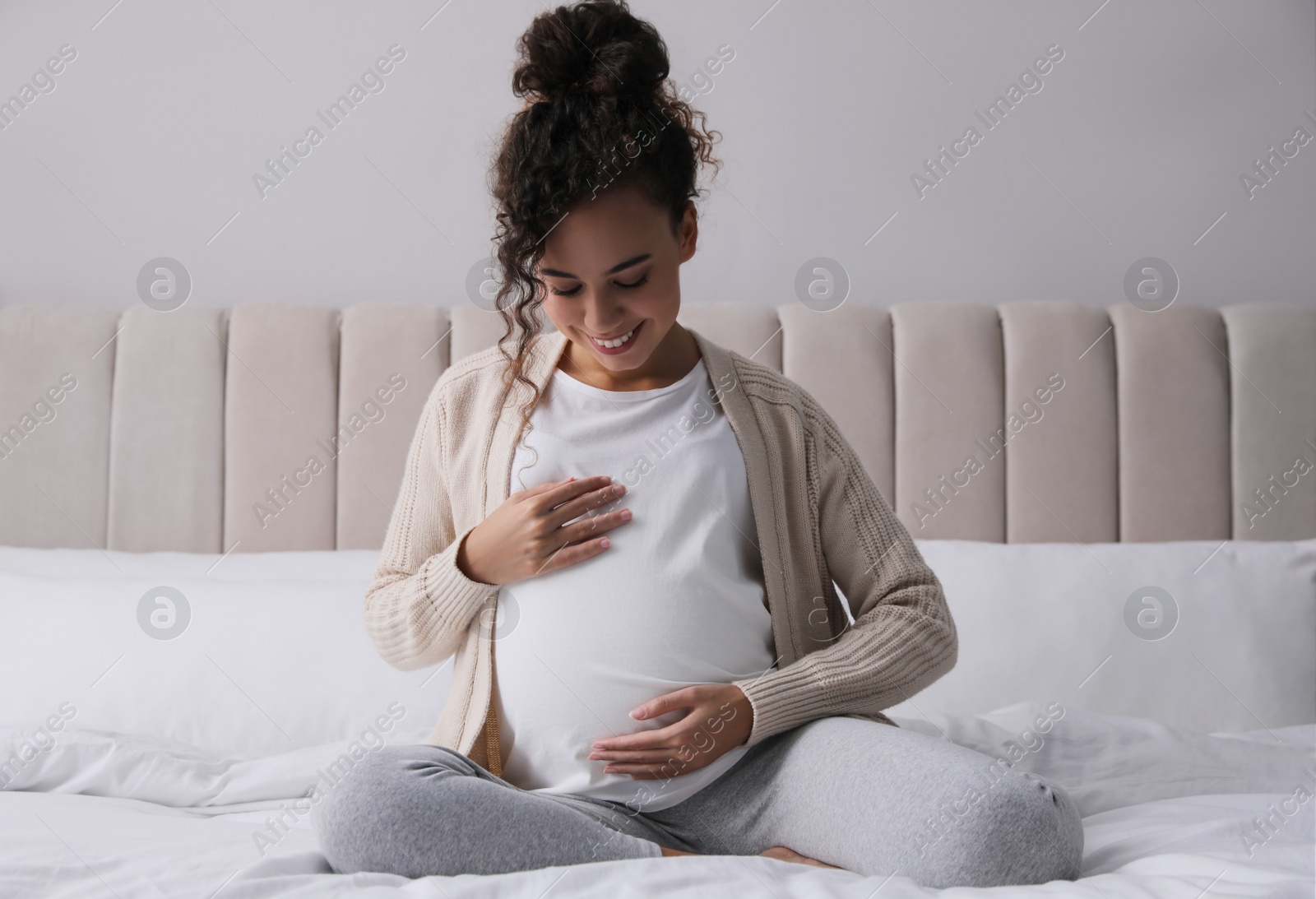 Photo of Pregnant young African-American woman sitting on bed at home