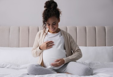 Pregnant young African-American woman sitting on bed at home