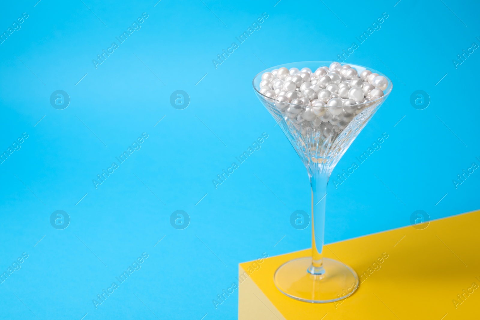 Photo of Beautiful martini glass with pearls on light blue background. Space for text