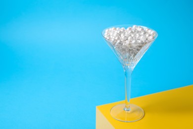 Photo of Beautiful martini glass with pearls on light blue background. Space for text