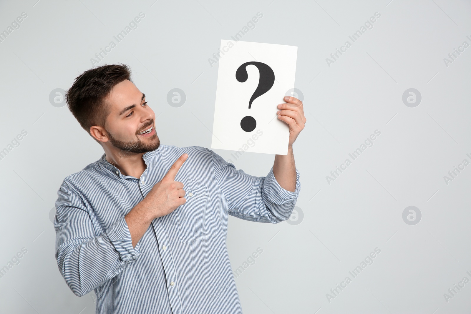 Photo of Happy man holding question mark sign on light background