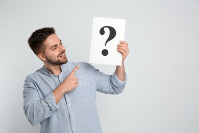 Photo of Happy man holding question mark sign on light background