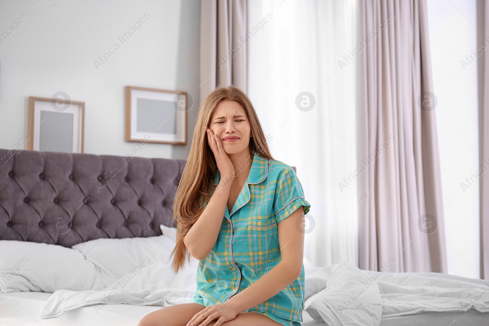 Photo of Young woman suffering from tooth pain in bedroom