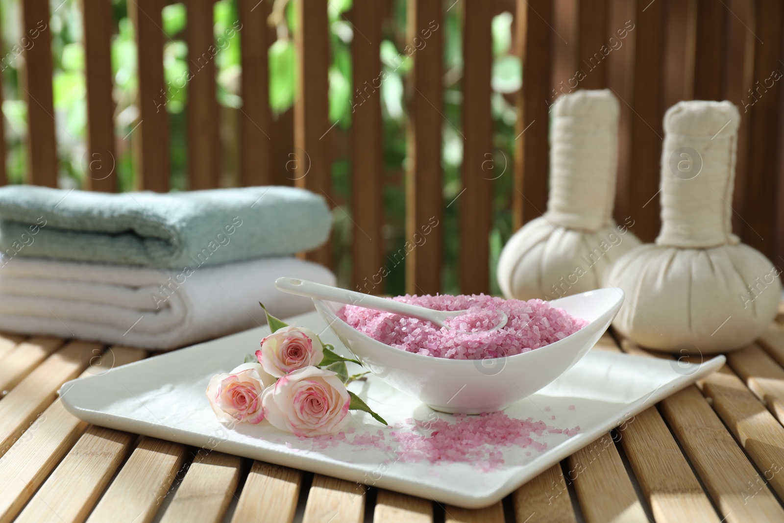 Photo of Bowl of pink sea salt and beautiful roses on wooden table, space for text