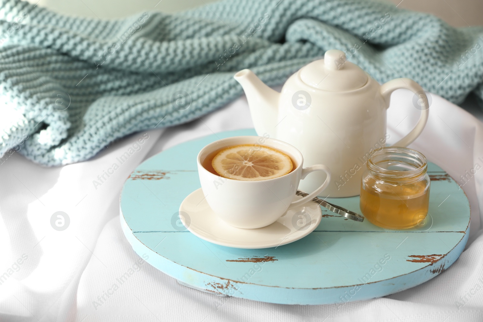 Photo of Wooden board with cup of lemon tea and teapot on fabric