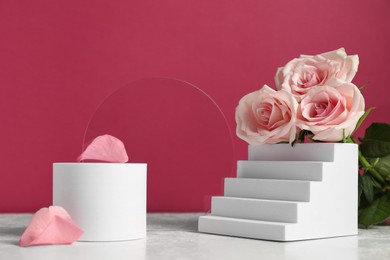 Stylish presentation of product. Beautiful roses and geometric figures on white table against pink background
