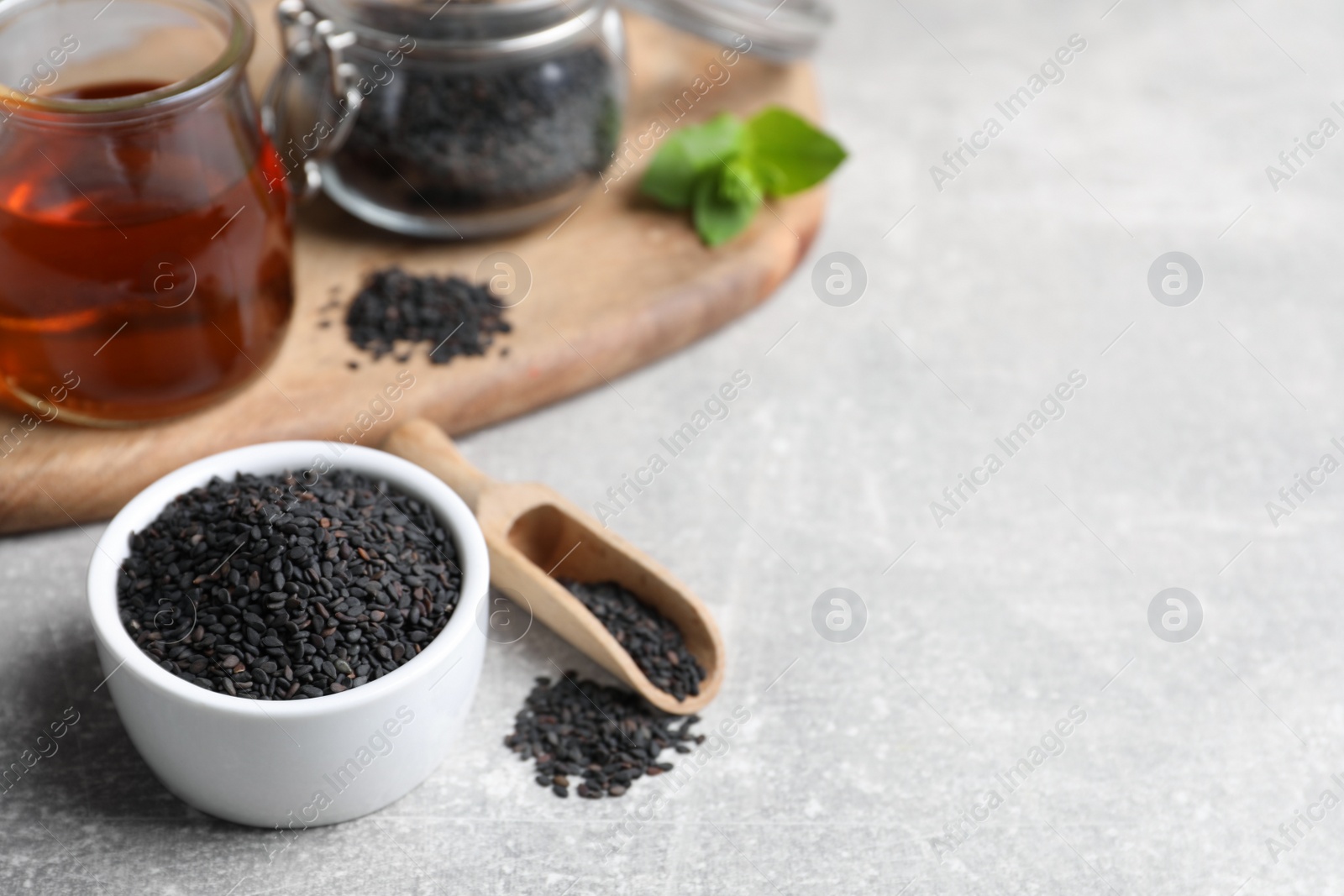 Photo of Black sesame seeds and oil on grey table, space for text