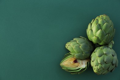 Photo of Cut and whole fresh raw artichokes on green background, flat lay. Space for text