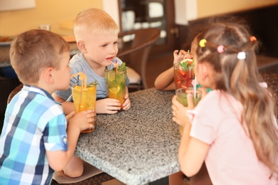 Photo of Cute children with glasses of natural lemonades at table in cafe