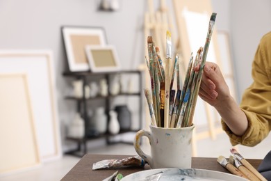 Woman taking brush from mug in studio, closeup. Space for text