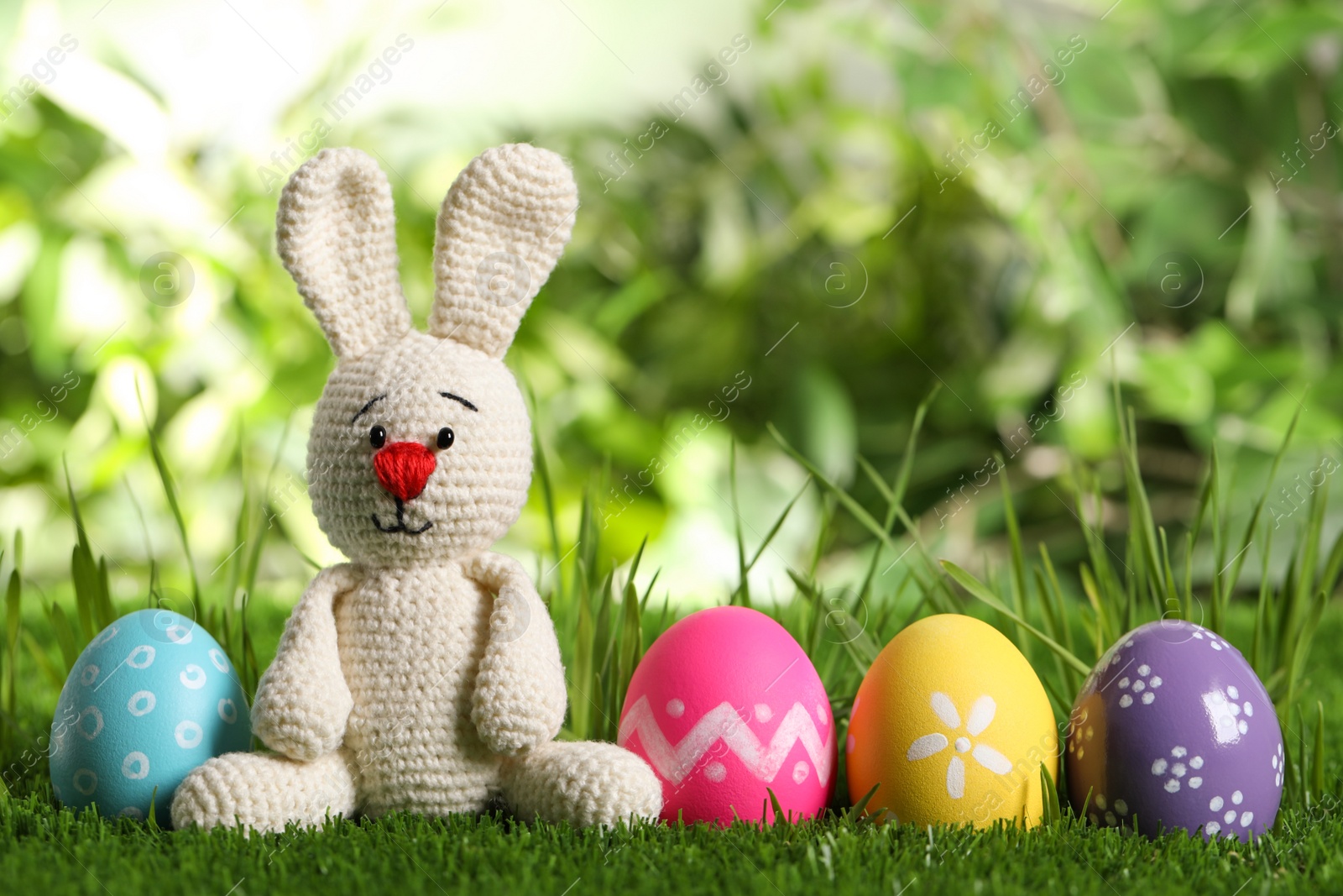 Photo of Colorful Easter eggs and toy rabbit on green grass. Space for text
