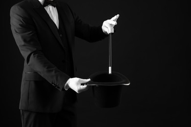 Photo of Magician showing magic trick with top hat on black background, closeup. Space for text