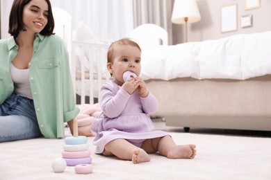 Photo of Cute baby girl playing with toy pyramid near mother on floor at home