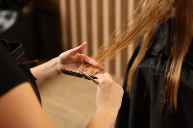 Professional hairdresser combing girl's hair in beauty salon, closeup
