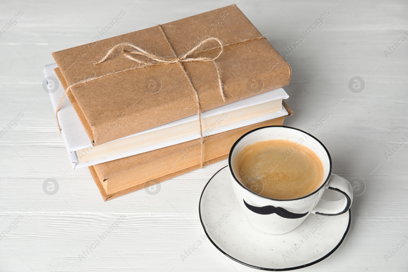 Photo of Cup with paper moustache and books on white wooden table. Happy Father's Day