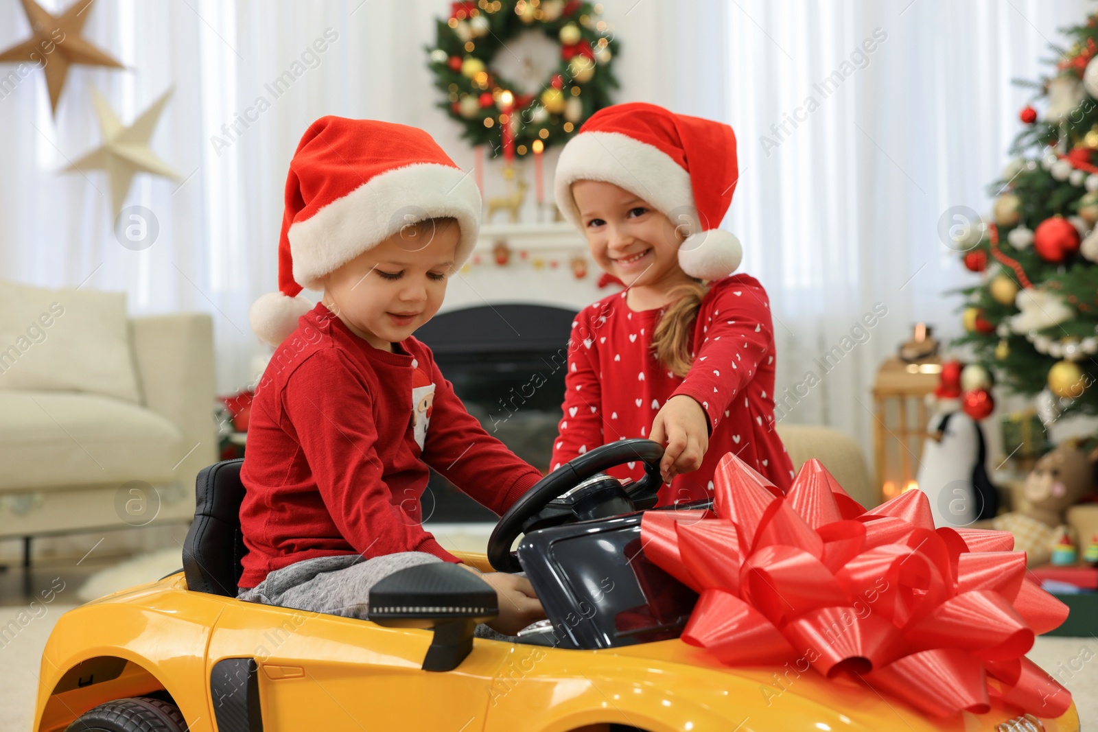 Photo of Cute little children playing with toy car in room decorated for Christmas