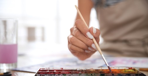 Image of Young woman drawing with watercolors at table indoors, closeup. Banner design