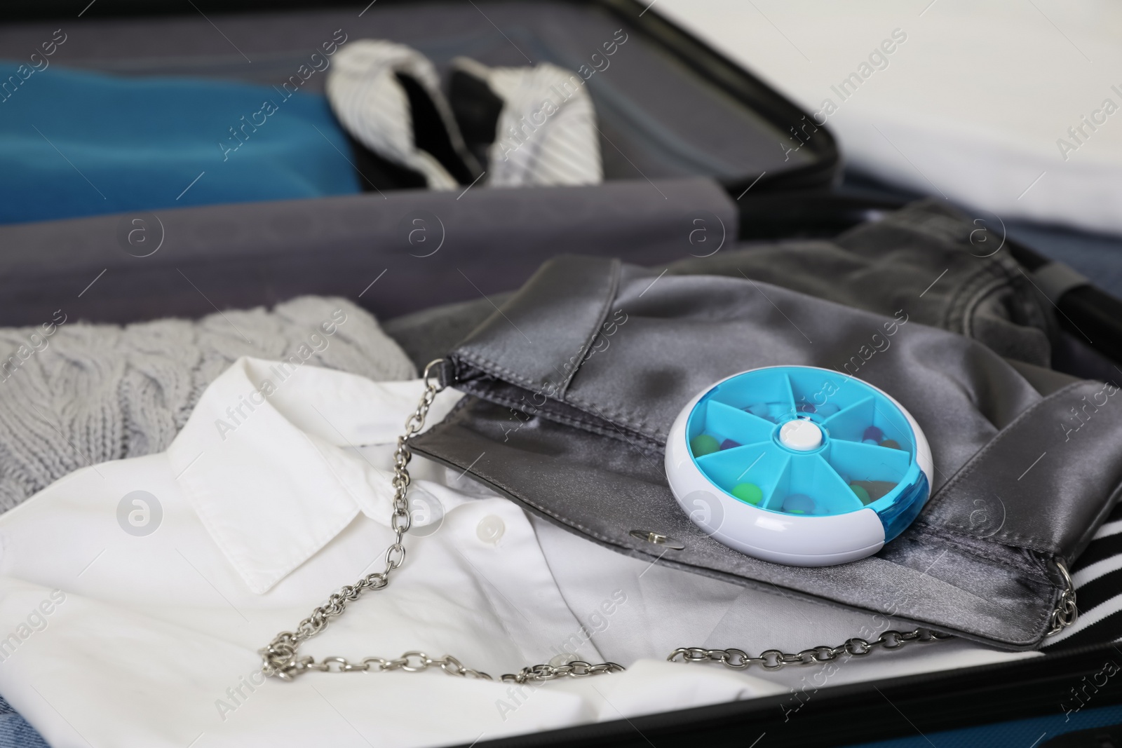 Photo of Open suitcase with packed clothes, accessories and pill box, closeup