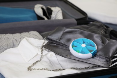 Open suitcase with packed clothes, accessories and pill box, closeup