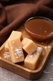 Yummy caramel candies, sauce and sea salt on brown table, closeup