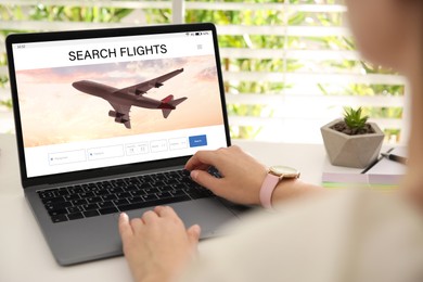 Image of Woman using laptop to book flight at white wooden table, closeup