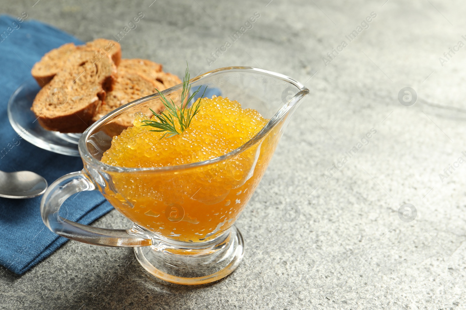 Photo of Fresh pike caviar in gravy boat, bread and spoon on grey table, closeup. Space for text