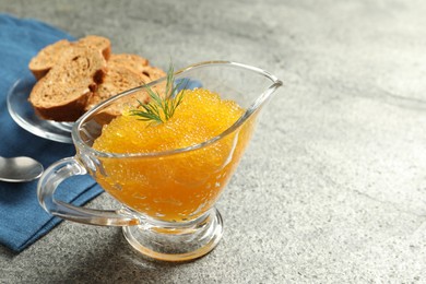 Photo of Fresh pike caviar in gravy boat, bread and spoon on grey table, closeup. Space for text