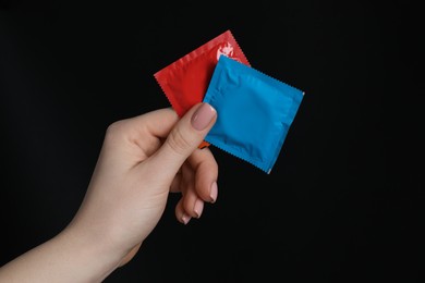 Photo of Woman holding condoms on black background, closeup