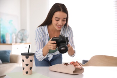 Photo of Young photographer taking picture of accessories indoors, focus on camera